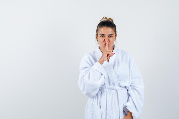 Young woman in bathrobe showing silence gesture and looking confident