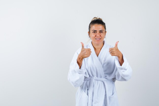 Young woman in bathrobe showing thumbs up and looking confident
