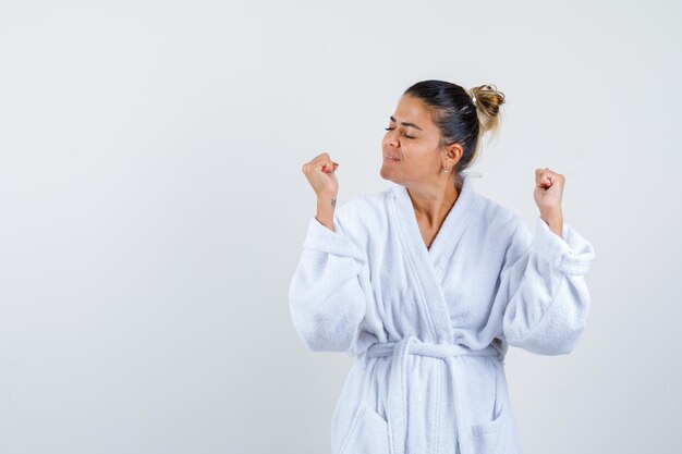 Young woman in bathrobe showing winner gesture and looking lucky