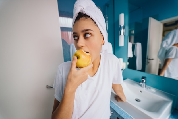 Молодая женщина в ванной, ест яблоко