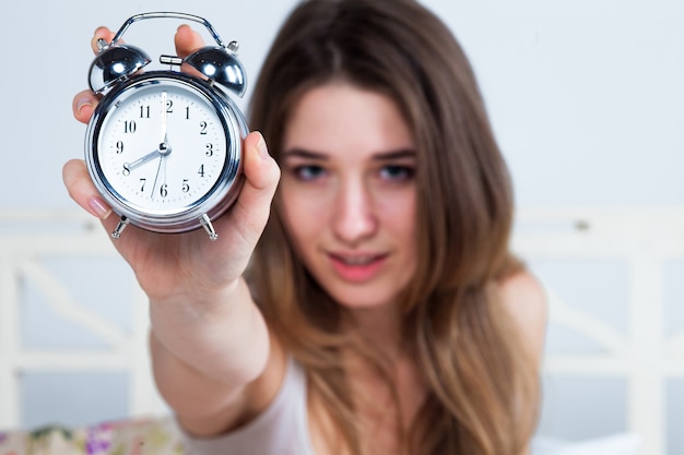 Young woman in bed with alarm clock