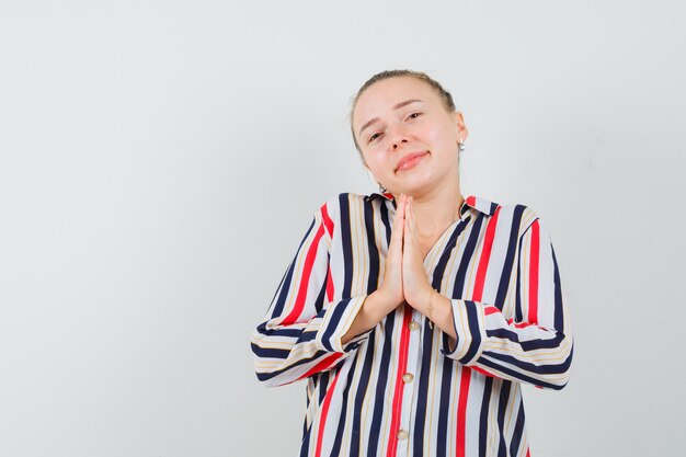 Young woman begging with obedient pleading expression in striped blouse and looking imploring