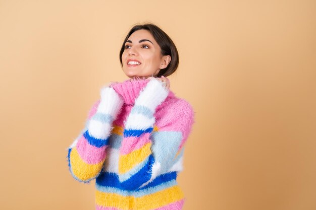 Молодая женщина на бежевом в ярком разноцветном уютном вязаном свитере мило улыбается