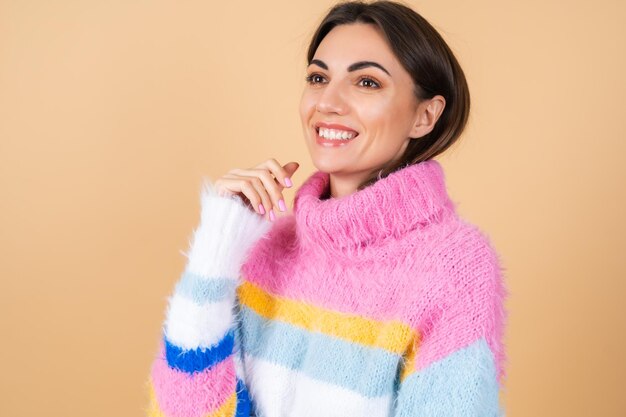 Молодая женщина на бежевом в ярком разноцветном уютном вязаном свитере мило улыбается