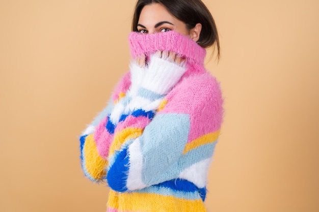 Young woman on beige in a bright multicolored cozy knitted sweater cute smiling