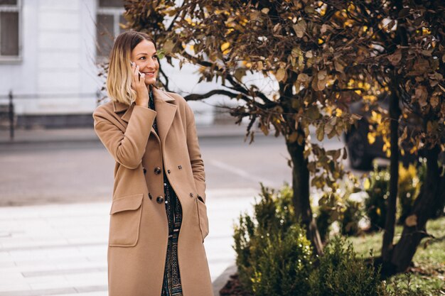 Young woman in beige coat using phone outside the street