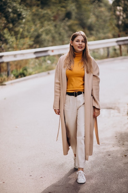 Young woman in beige coat walking in park