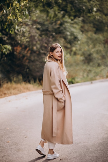 Young woman in beige coat walking in park