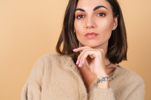 Young woman on beige in a soft cozy sweater with daytime professional make-up cute smiling