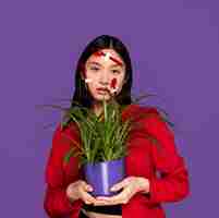 Free photo young woman being covered in plastic spoons and forks while holding a plant