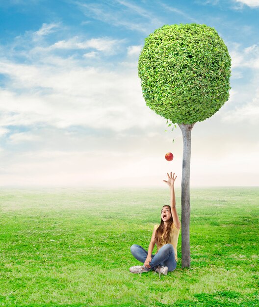 young woman being surprised by a red apple under a tree