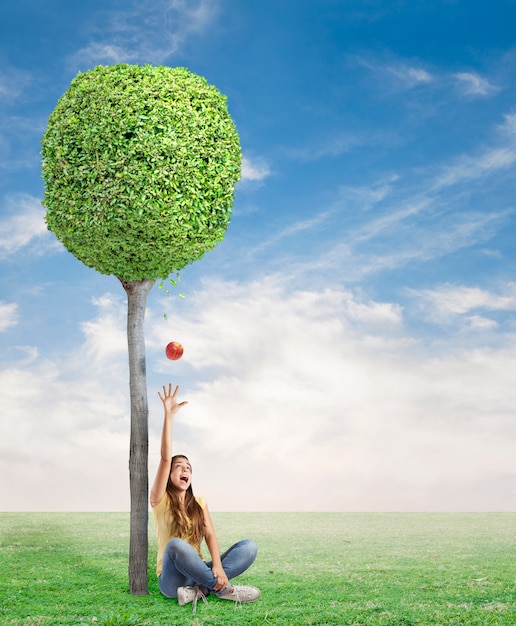 Free photo young woman being surprised by a red apple under a tree