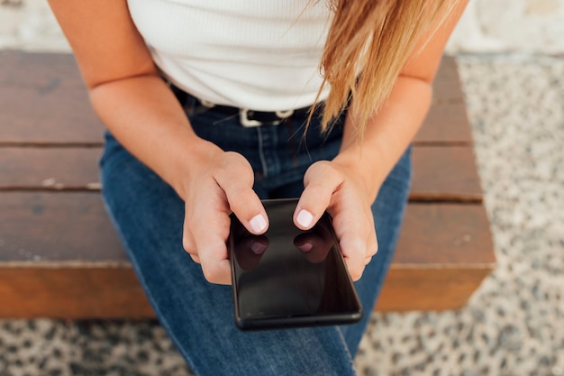 Foto gratuita giovane donna su un banco che manda un sms sullo smartphone