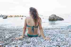 Foto gratuita giovane donna in bikini che si siede vicino al mare in spiaggia