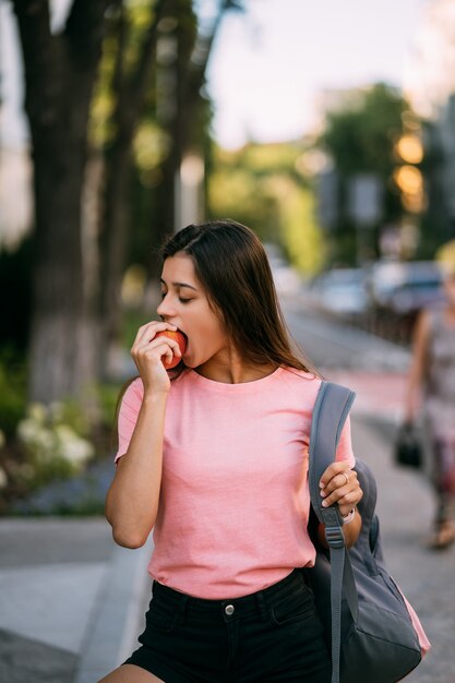 通りの背景にリンゴを噛む若い女性
