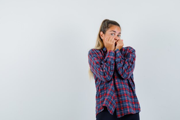 Young woman biting fists in checked shirt and looking scared