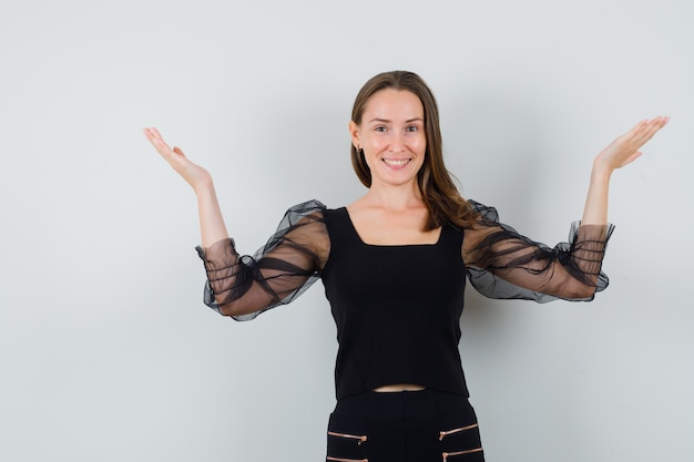 Young woman in black blouse and black pants holding hands like raising something and looking happy 