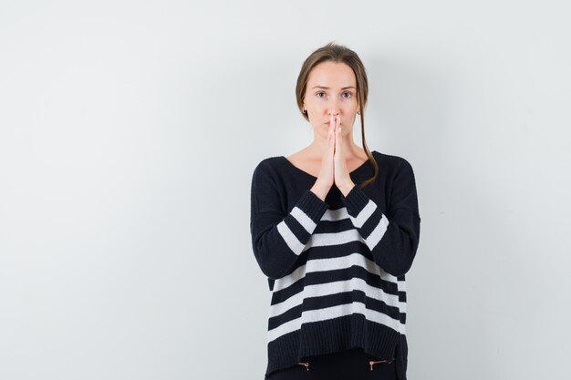 Young woman in black blouse and black pants standing in prayer pose and looking focused