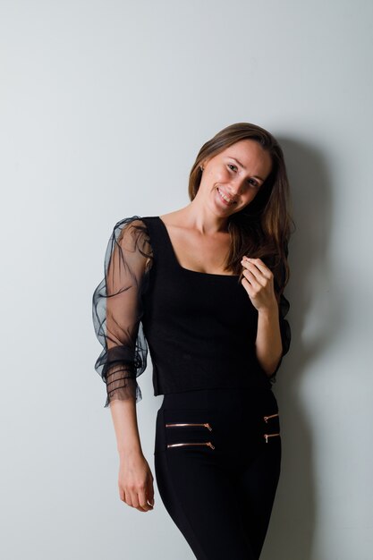 Young woman in black blouse and black pants standing straight and smiling gracefully and looking charming