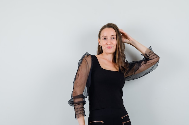 Young woman in black blouse holding hand on her head and looking confident 