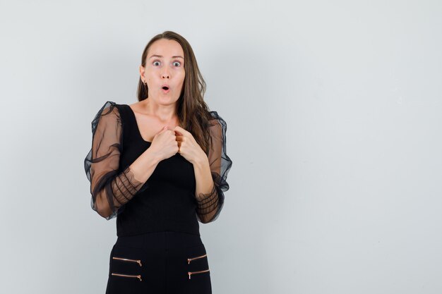 Young woman in black blouse holding hands on her chest and looking scared 