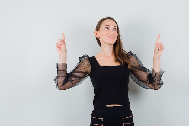 Young woman in black blouse pointing up and looking glad 