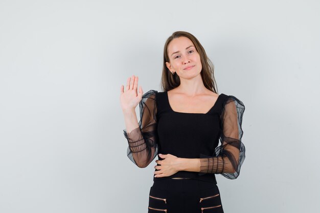 Young woman in black blouse showing goodbye gesture and looking calm 