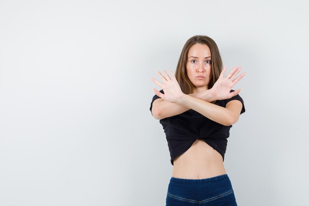 Foto gratuita giovane donna in camicetta nera che mostra il gesto di arresto con le braccia incrociate e che sembra seria