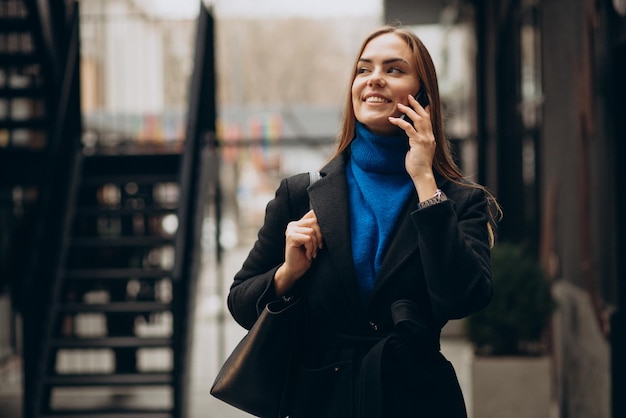 Молодая женщина в черном пальто с помощью телефона