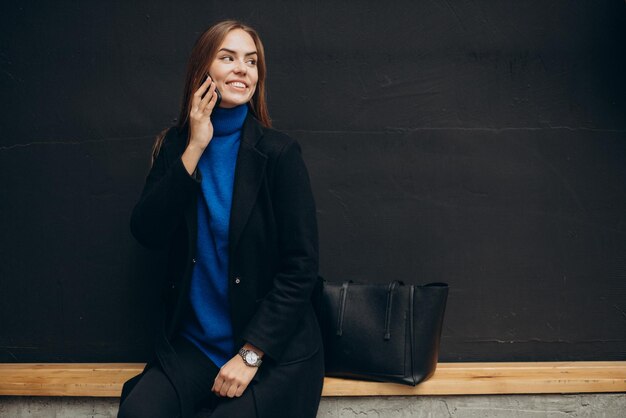 Young woman in black coat using phone