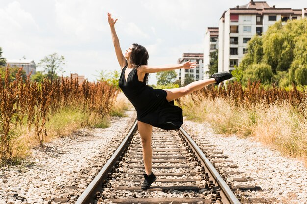 Young woman in black dress dancing at railroad