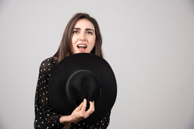 Молодая женщина в черном платье держит шляпу против ее тела.