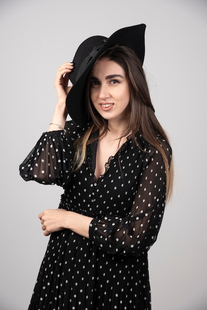 Young woman in black dress holding her hat.