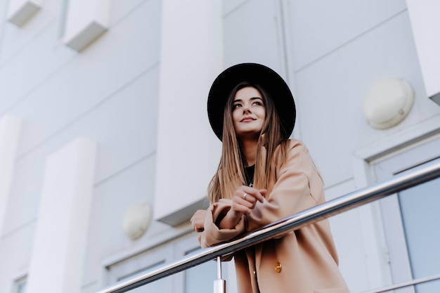 Young woman in black hat sitting at the handrail the building in the city