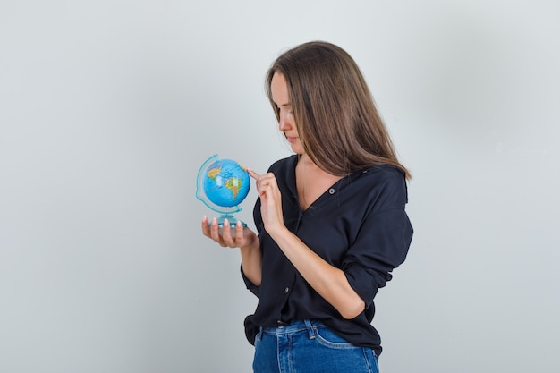 Young woman in black shirt, jeans shorts choosing destination on globe with finger
