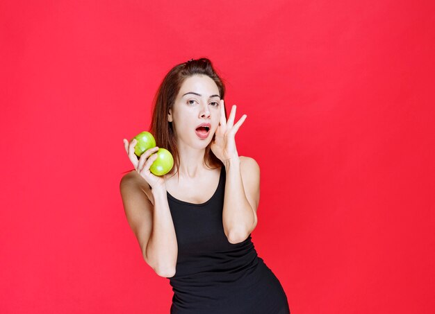 Young woman in black singlet holding green apples and looks surprised