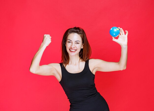 Young woman in black singlet holding a mini world globe and feeling strong