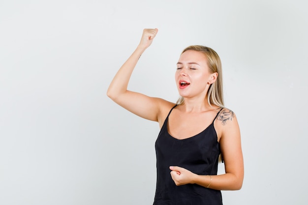 Giovane donna in canottiera nera alzando la mano con il pugno chiuso e guardando felice