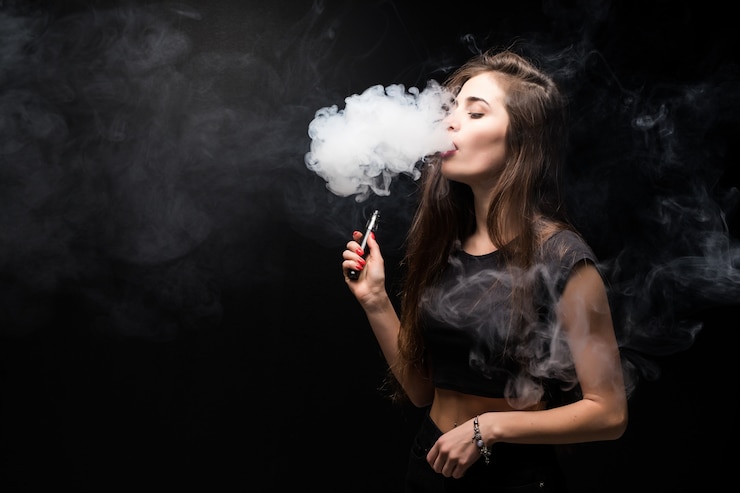 Free Photo young woman in black smokes an electronic cigarette on dark wall
