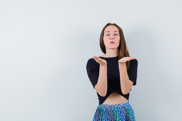 Young woman in black t-shirt and blue skirt sending kisses to camera and looking attractive