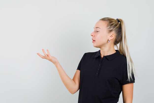 Young woman in black t-shirt gesturing like holding something and looking attractive