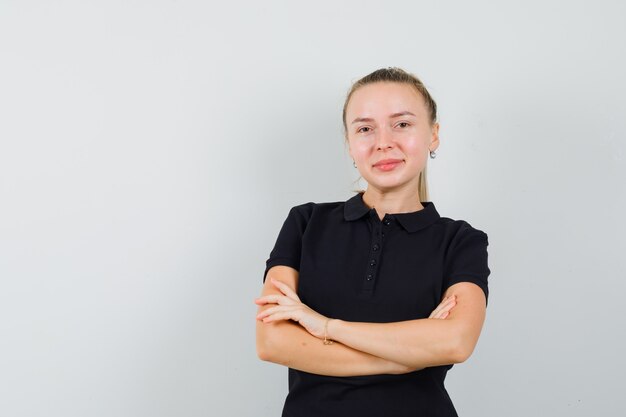 Young woman in black t-shirt standing with crossed arms and smiling and looking happy