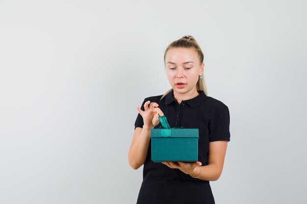 Young woman in black t-shirt trying to open gift and looking pretty