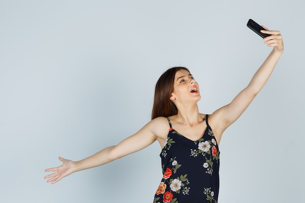 Young woman in blouse posing while taking selfie on smartphone and looking relaxed , front view.