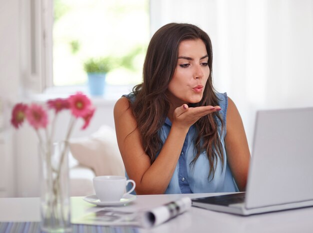 Young woman blowing air kiss to laptop computer. Video conference concept