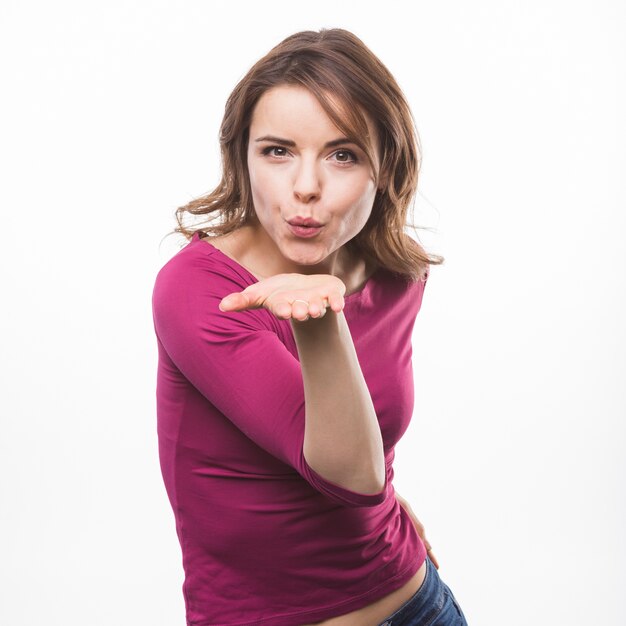 Young woman blowing flying kiss against white background