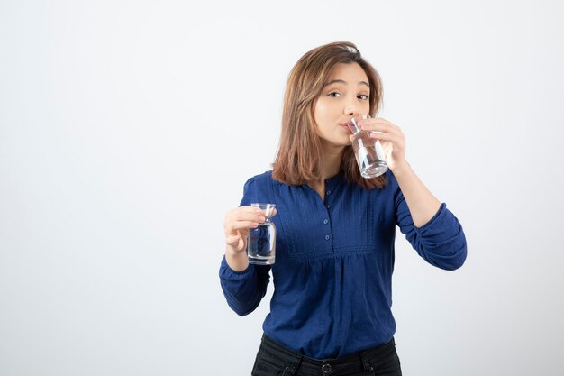 Young woman in blue blouse drinking glass of water. 