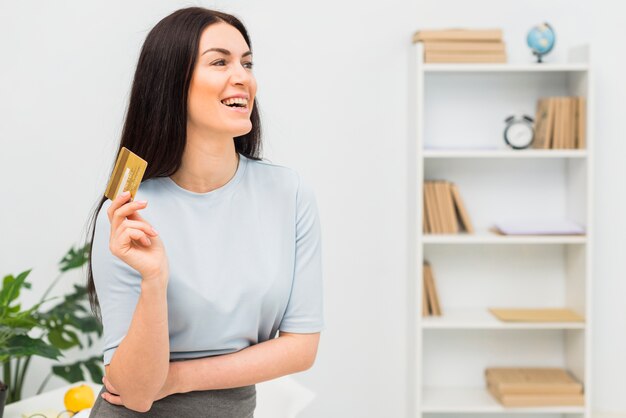 Young woman in blue clothes standing with credit card in office 