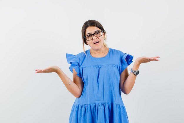 Young woman in blue dress showing helpless gesture and looking confused