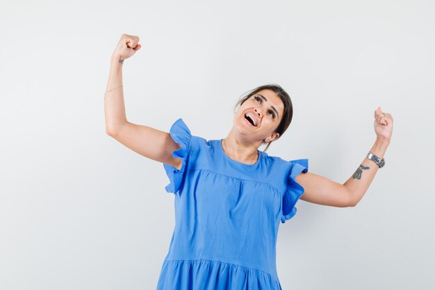 Young woman in blue dress showing winner gesture and looking blissful